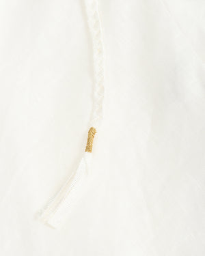 Close-up detail of a white textured garment with a braided drawstring and a small gold decorative accent.