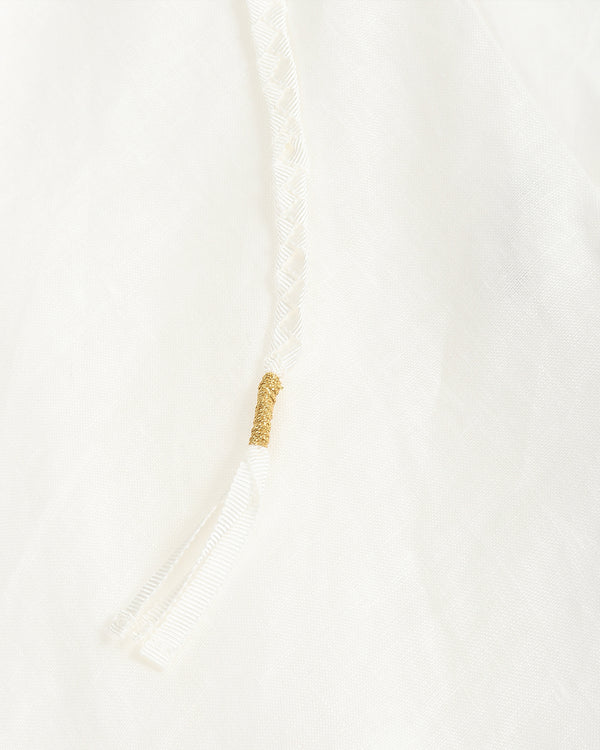 Close-up detail of a white textured garment with a braided drawstring and a small gold decorative accent.