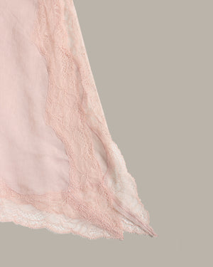 A close-up of a light pink sheer fabric with delicate lace trim, shown against a solid taupe-gray background.