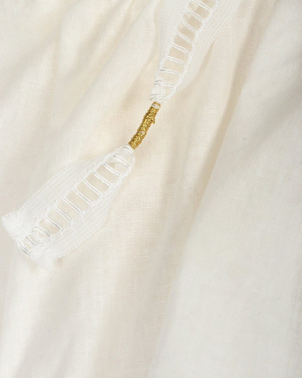 Close-up of a white garment with a gold accent straps on a beige background
