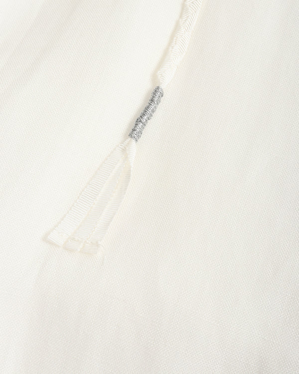 Close-up of a white textured fabric garment with a drawstring detail and a small gray embroidered accent.