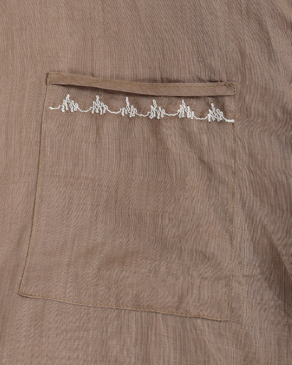 Close-up of a taupe-brown textured fabric garment featuring a front pocket with a decorative row of white embroidered details along the top edge.
