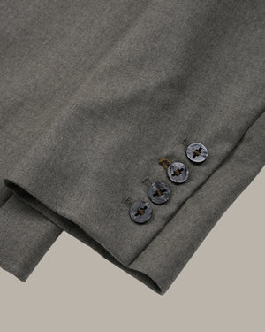 Close-up of a folded gray wool-blend blazer sleeve showing the buttoned cuff and fabric texture against a solid neutral background.