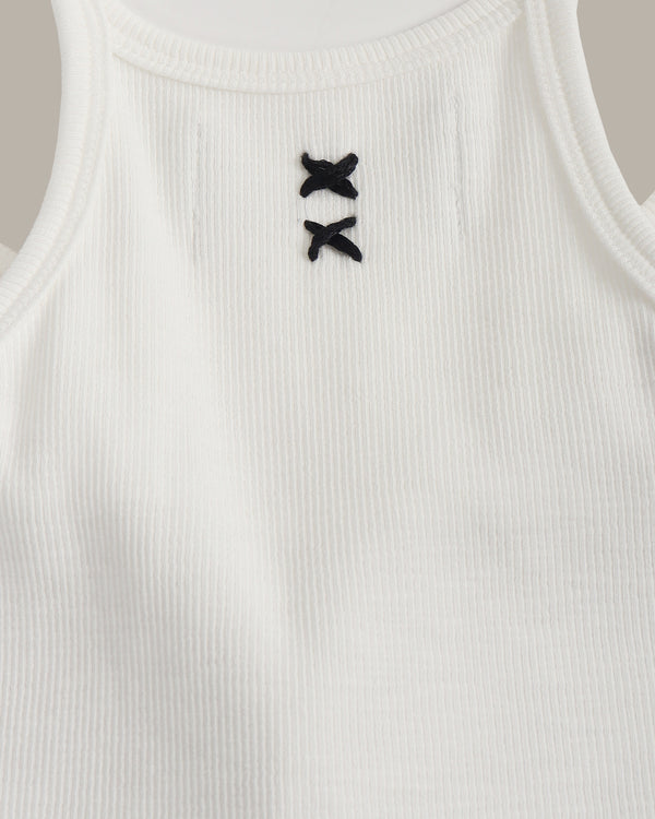 White ribbed tank top with black decorative buttons on a neutral background
