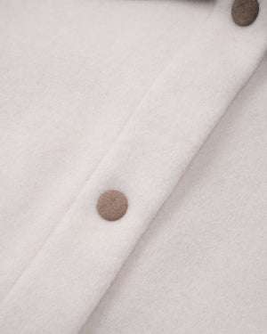 Close-up of a cream-colored wool or cashmere fabric with a diagonal button placket and two visible taupe buttons.