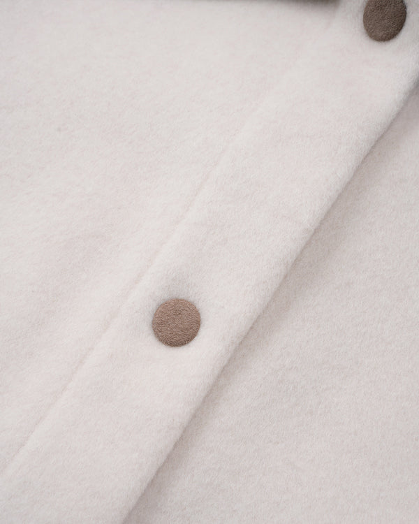 Close-up of a cream-colored wool or cashmere fabric with a diagonal button placket and two visible taupe buttons.