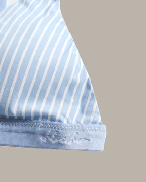 Close-up of a light blue and white striped fabric product, showing a curved edge with fine stitching and a small embroidered logo on the hem, against a solid beige background.