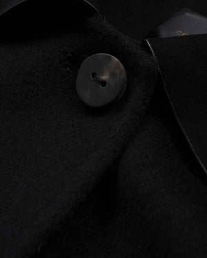 Close-up detail of a black wool-like garment with a single dark button and a folded collar.