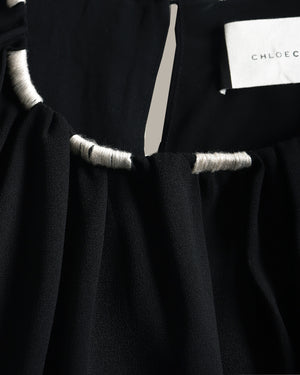 Close-up of a black top with gathered fabric and contrasting light gray trim, showing a white brand label that reads CHLOE.