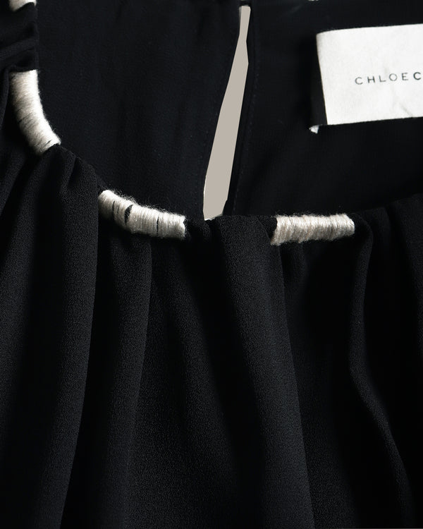 Close-up of a black top with gathered fabric and contrasting light gray trim, showing a white brand label that reads CHLOE.