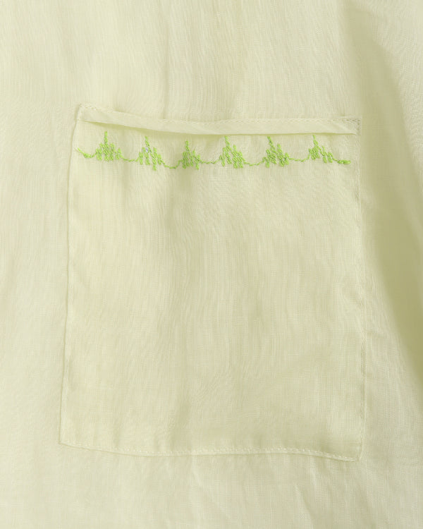 Close-up of a light cream or off-white fabric garment with a rectangular patch pocket featuring a row of small lime green embroidered details along the top edge.