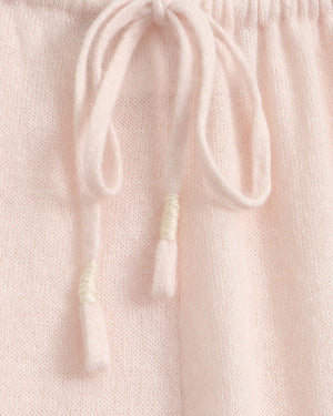 Close-up of a light pink knit fabric with a matching drawstring and tassel detail.