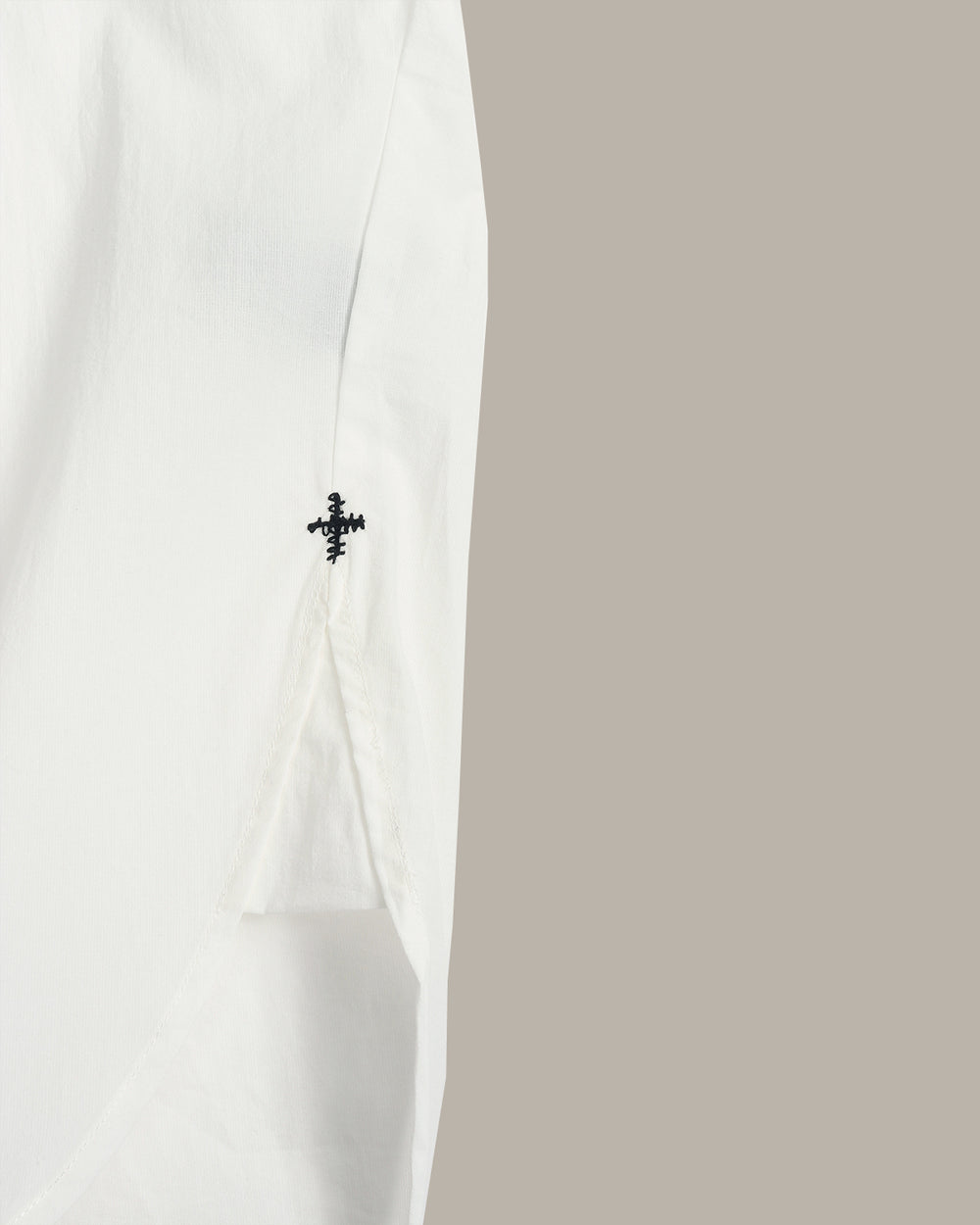 An  white, loose-fitting short-sleeve top with a high-low hem and small black embroidered crosses on the sides, displayed flat against a solid taupe background.