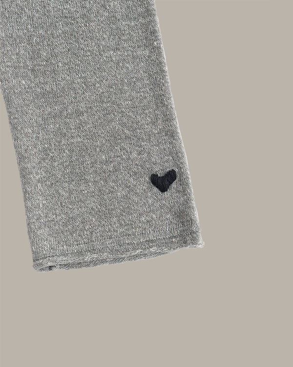 Close-up of a heather gray knit fabric sleeve or cuff with a small black heart embroidered near the cuff edge, shown against a solid taupe background.