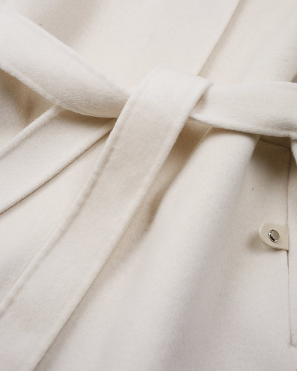 Close-up of an off-white or cream-colored fabric garment with a matching tie belt and a small button detail.