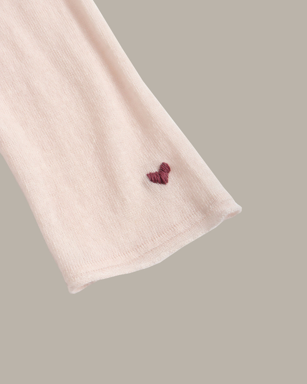 A pale blush pink long-sleeve crewneck knit top, shown flat against a solid taupe-gray background.