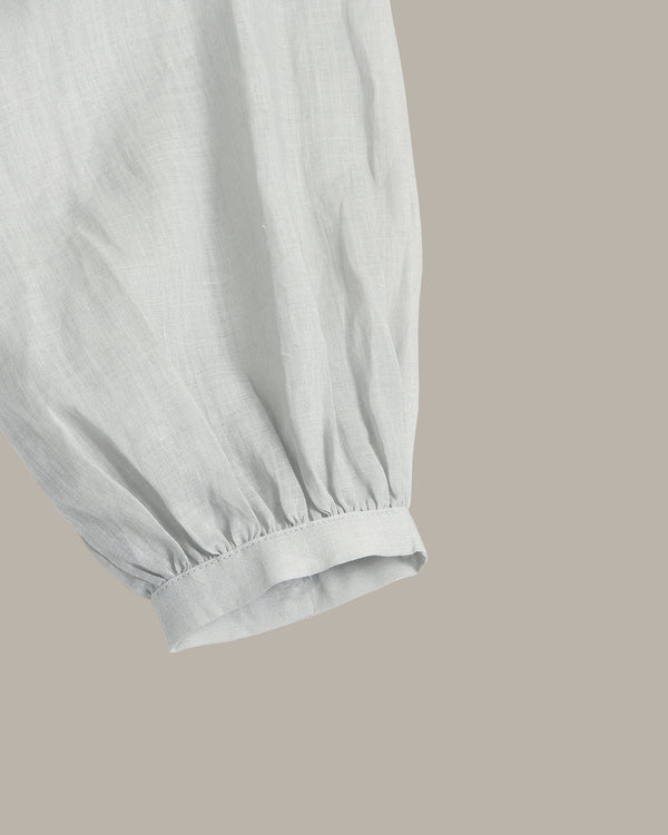 Close-up of a light gray fabric garment sleeve with gathered elastic cuffs, shown against a solid taupe background.