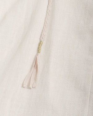 Close-up of a light cream or off-white textured fabric with a thin braided drawstring in a pale blush tone and a small gold-toned decorative accent.