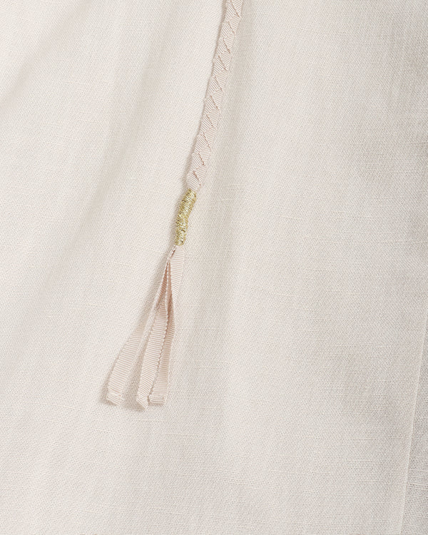 Close-up of a light cream or off-white textured fabric with a thin braided drawstring in a pale blush tone and a small gold-toned decorative accent.