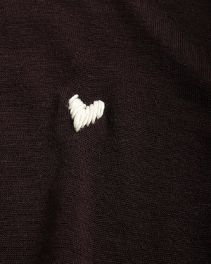Close-up of a dark brown knit fabric with a small white embroidered heart on the chest.