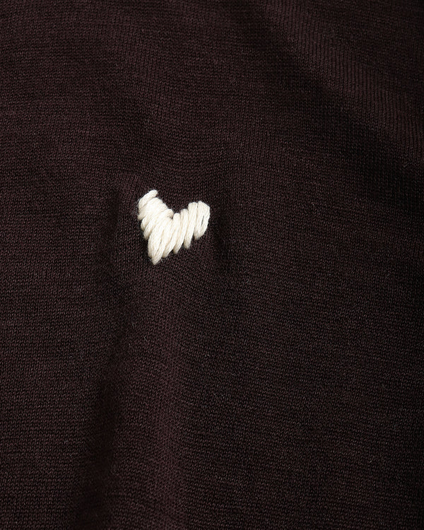 Close-up of a dark brown knit fabric with a small white embroidered heart on the chest.