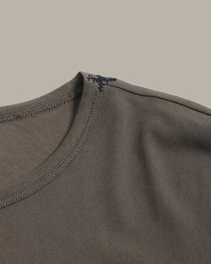 Close-up detail of a crewneck t-shirt showing the ribbed collar, double-stitched edge, and a small decorative embroidered cross on the inside neckline.