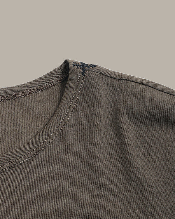 Close-up detail of a crewneck t-shirt showing the ribbed collar, double-stitched edge, and a small decorative embroidered cross on the inside neckline.