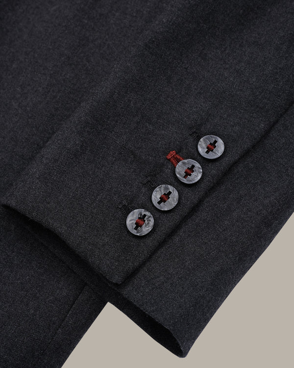 Close-up of a dark charcoal gray wool suit jacket sleeve, showing three buttons with a red center and a small red thread accent.
