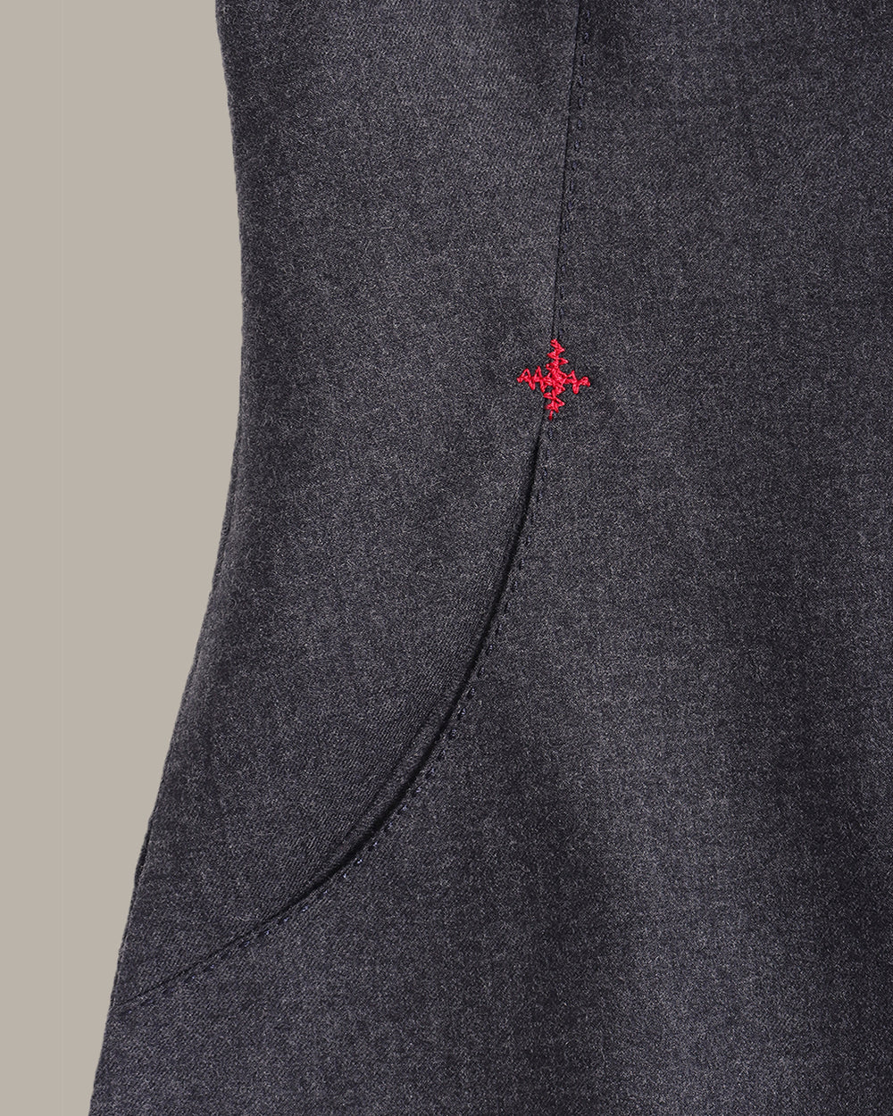 A sleeveless dark gray textured vest with a round neckline, front pockets, and small red embroidered star details on the sides, shown against a solid beige background.