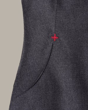 Close-up of a dark gray textured fabric garment with a curved seam and a small red embroidered cross logo near the upper right side.