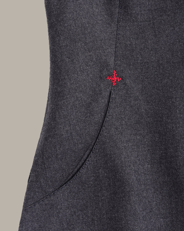 Close-up of a dark gray textured fabric garment with a curved seam and a small red embroidered cross logo near the upper right side.
