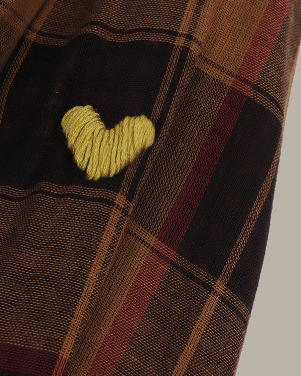 Close-up of a plaid fabric with a green heart-shaped object on a neutral background