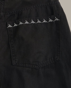 Close-up of a black denim pocket with a white embroidered heartbeat line across the top, set against a neutral gray background.