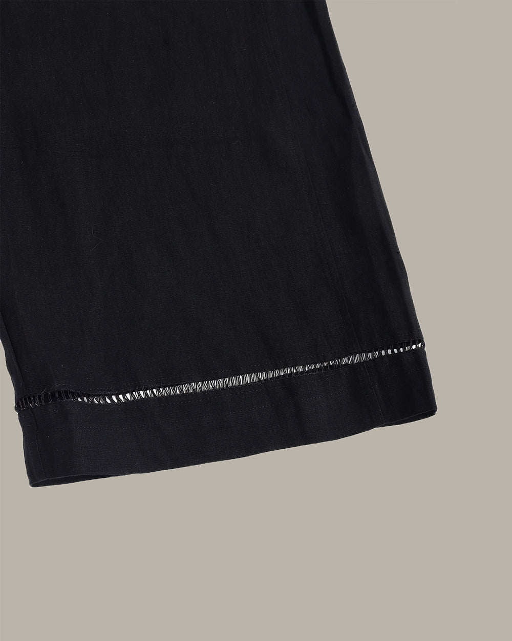 Black wide-leg cropped pants with an elastic waistband and subtle contrast stitching at the hems, shown flat against a solid taupe background.