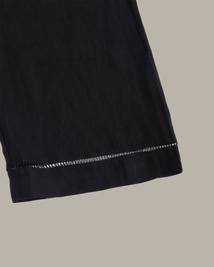 Close-up of a black garment hem with a decorative trim, shown against a solid taupe background.