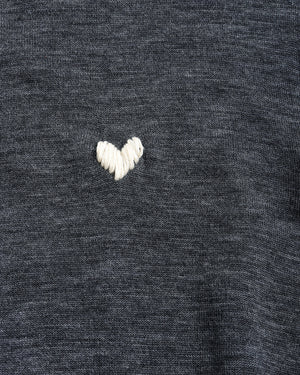 Close-up of a dark heather gray knit fabric with a small white embroidered heart on the chest.
