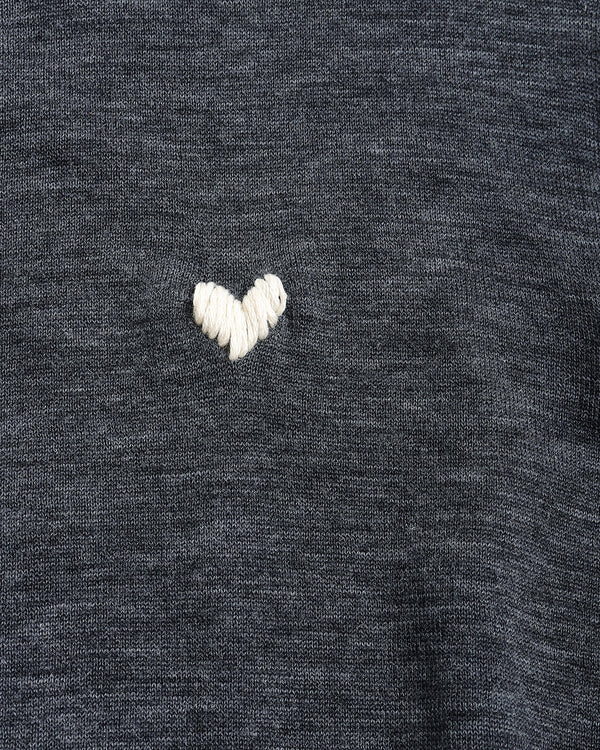 Close-up of a dark heather gray knit fabric with a small white embroidered heart on the chest.