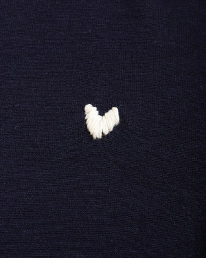 Close-up of a dark navy knit fabric with a small white embroidered heart on the chest.