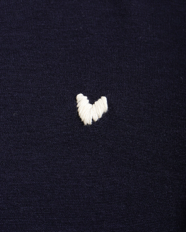 Close-up of a dark navy knit fabric with a small white embroidered heart on the chest.