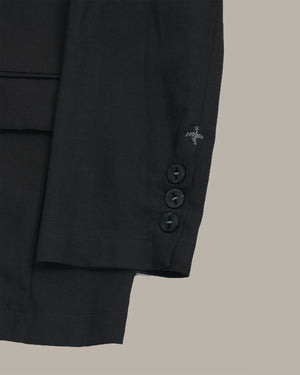 Close-up of a black suit jacket sleeve with cross stitching details and buttons on a beige background