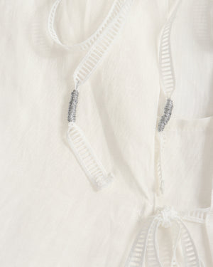 Close-up of a white textured fabric garment with white drawstrings and small silver bead accents.