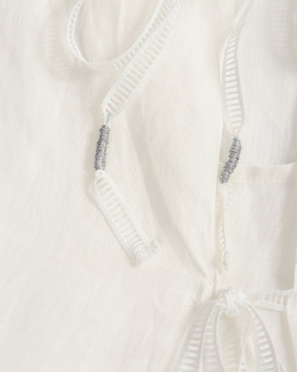 Close-up of a white textured fabric garment with white drawstrings and small silver bead accents.