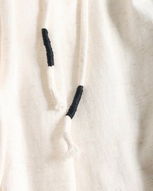 Close-up of a cream-colored textured fabric garment with black embroidered drawstring tips.