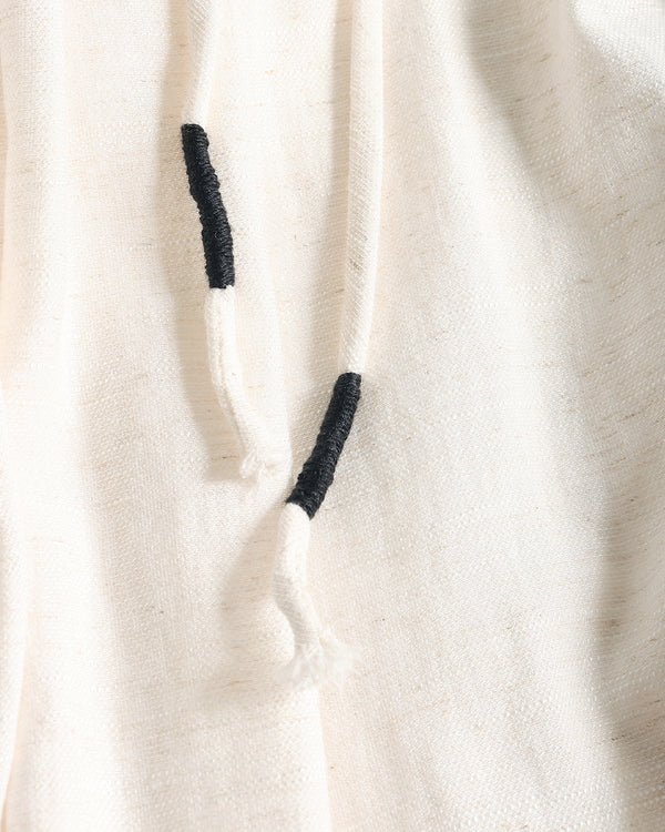 Close-up of a cream-colored textured fabric garment with black embroidered drawstring tips.