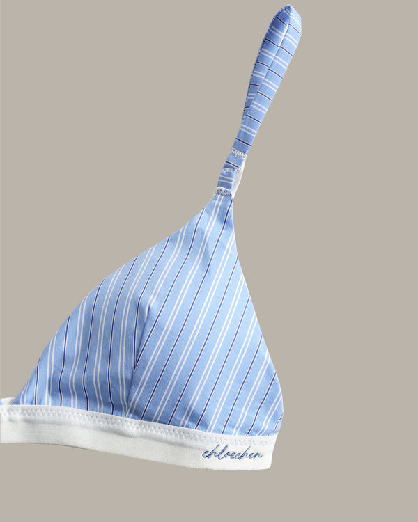 A light blue and white striped bralette with a white underband and a small embroidered brand name on the front, shown against a solid taupe background.
