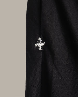 Close-up of a black textured garment with a small white embroidered logo on the side, set against a solid light gray background.
