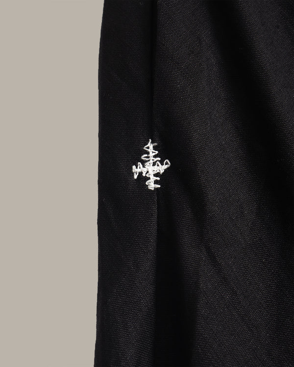 Close-up of a black textured garment with a small white embroidered logo on the side, set against a solid light gray background.