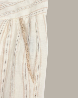 Close-up of a cream-colored woven textile with vertical beige stripes and a braided cord detail, shown against a plain taupe background.