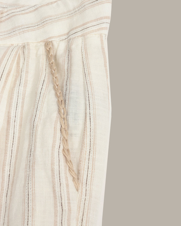 Close-up of a cream-colored woven textile with vertical beige stripes and a braided cord detail, shown against a plain taupe background.