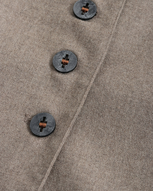 Close-up of a textured taupe wool coat with three dark buttons featuring copper-colored centers, showing the fine fabric weave and diagonal seam.
